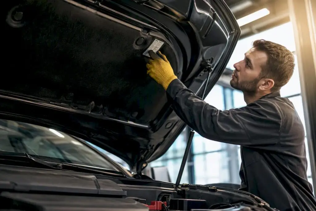 Technician locating refrigerant sticker under hood