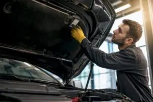 Technician locating refrigerant sticker under hood